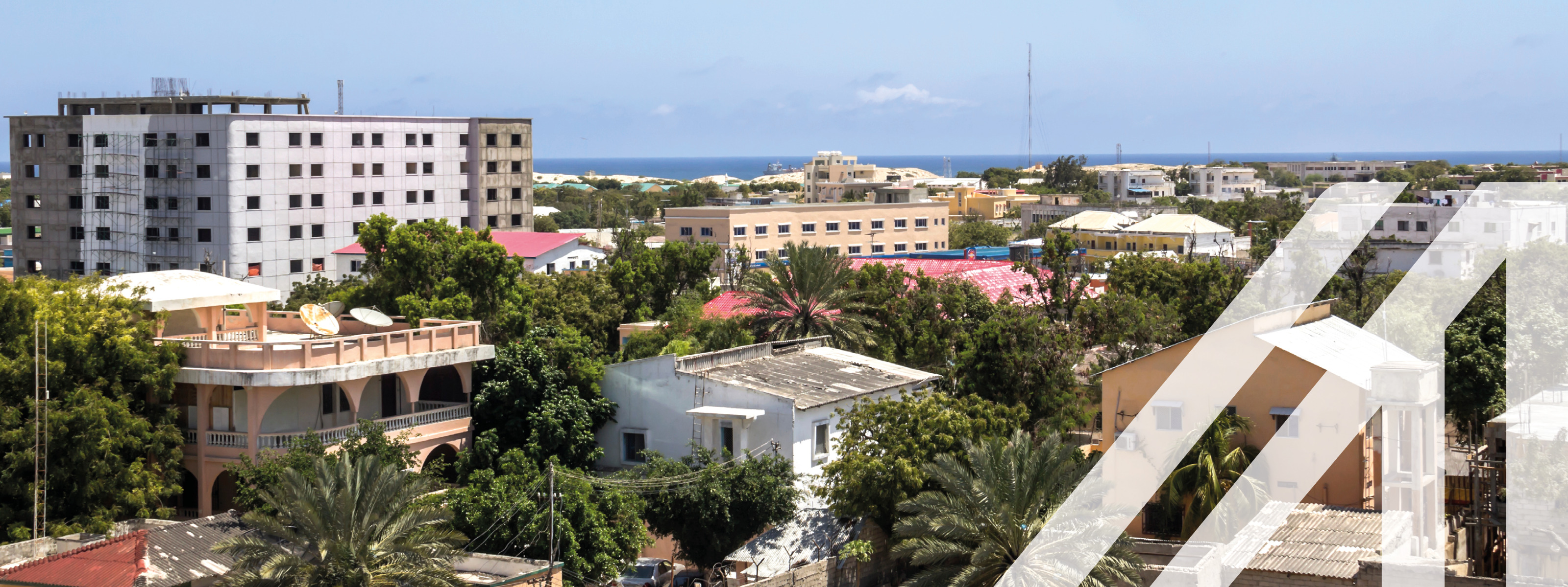 Stadtansicht von Mogadischu, Hauptstadt von Somalia: Zwischen Häusern Bäume, im Hintergrund Meer unter blauem Himmel
