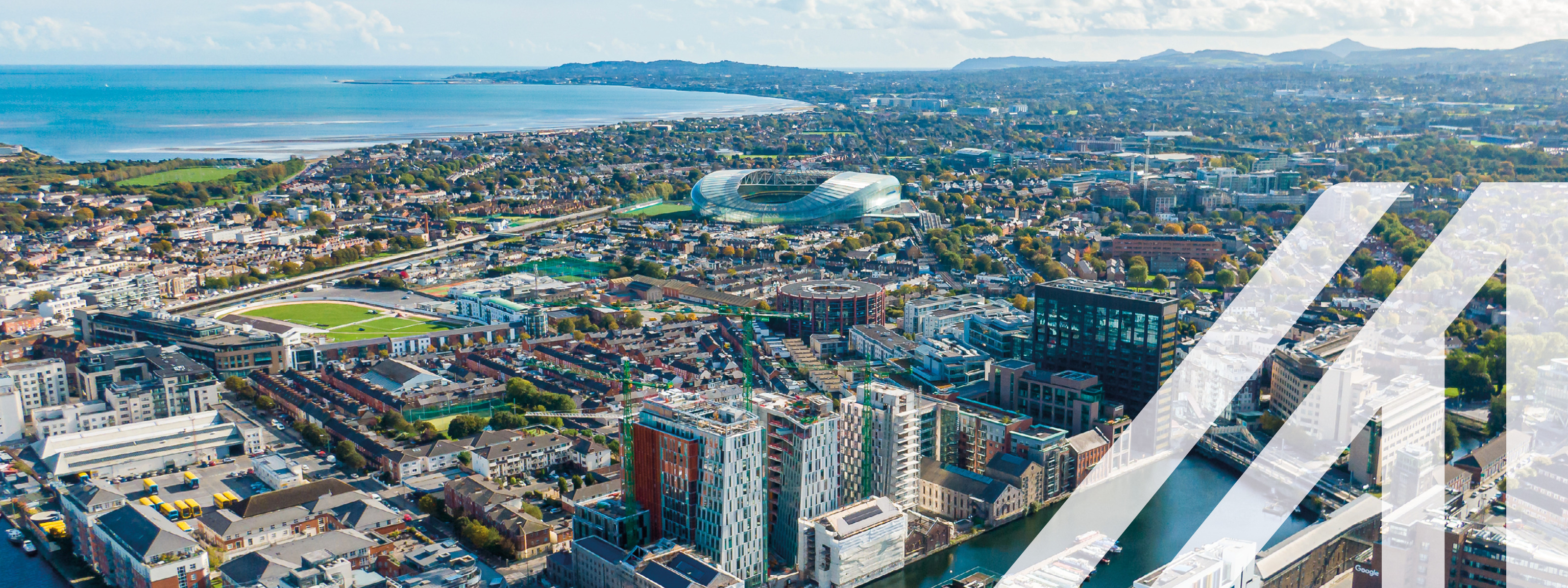 Luftaufnahme von Dublin mit Blick auf den Hafen und moderne Gebäude, im Hintergrund sieht man das Meer und Wolken am Himmel