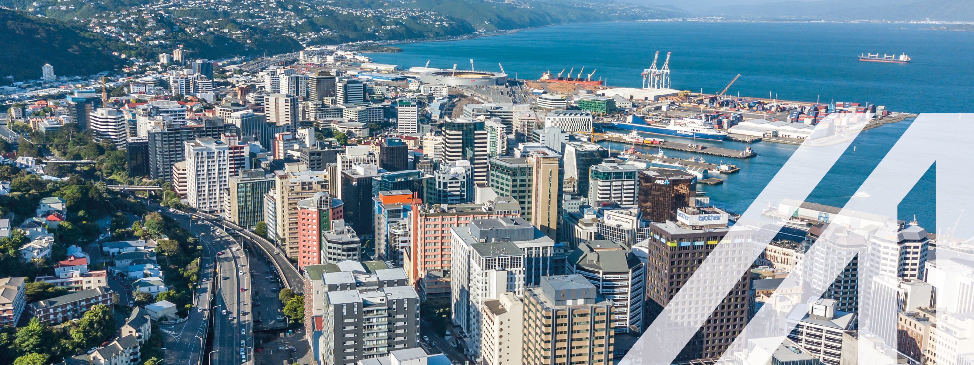 Blick auf Wellington, Neuseeland, und den Central Business District, mit vielen Wolkenkratzern, Hafen, Meer und Bergkette im Hintergrund<br />
