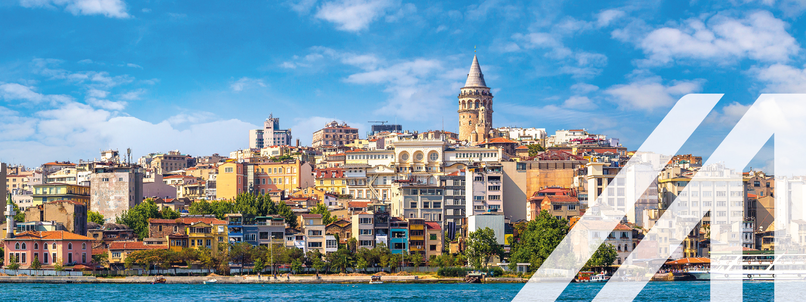 Stadtansicht von Istanbul: bunte Häuser am Wasser, in der MItte ragt der Galata Tower empor, blauer Himmel mit einigen Wolken. Über das Bild wurde ein weißes Austria A gelegt.