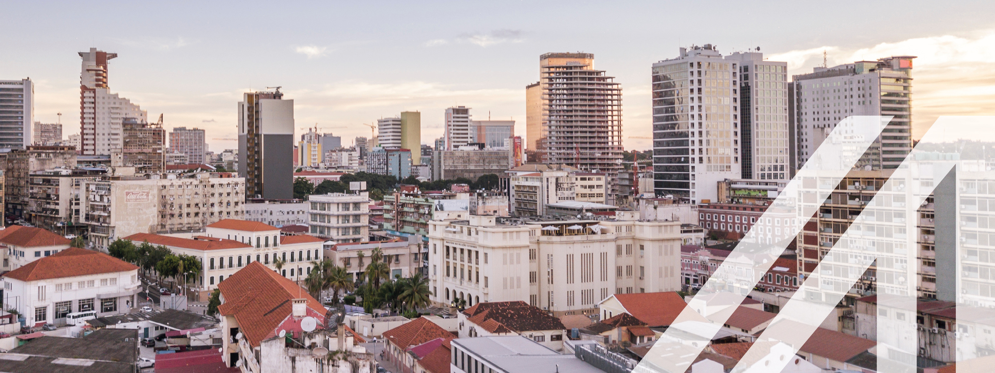 Blick auf Luanda, Hauptstadt von Agola. Man sieht im Vordergrund historische weiße Häuser mit roten Dächern, im Hintergrund Wolkenkratzer.
