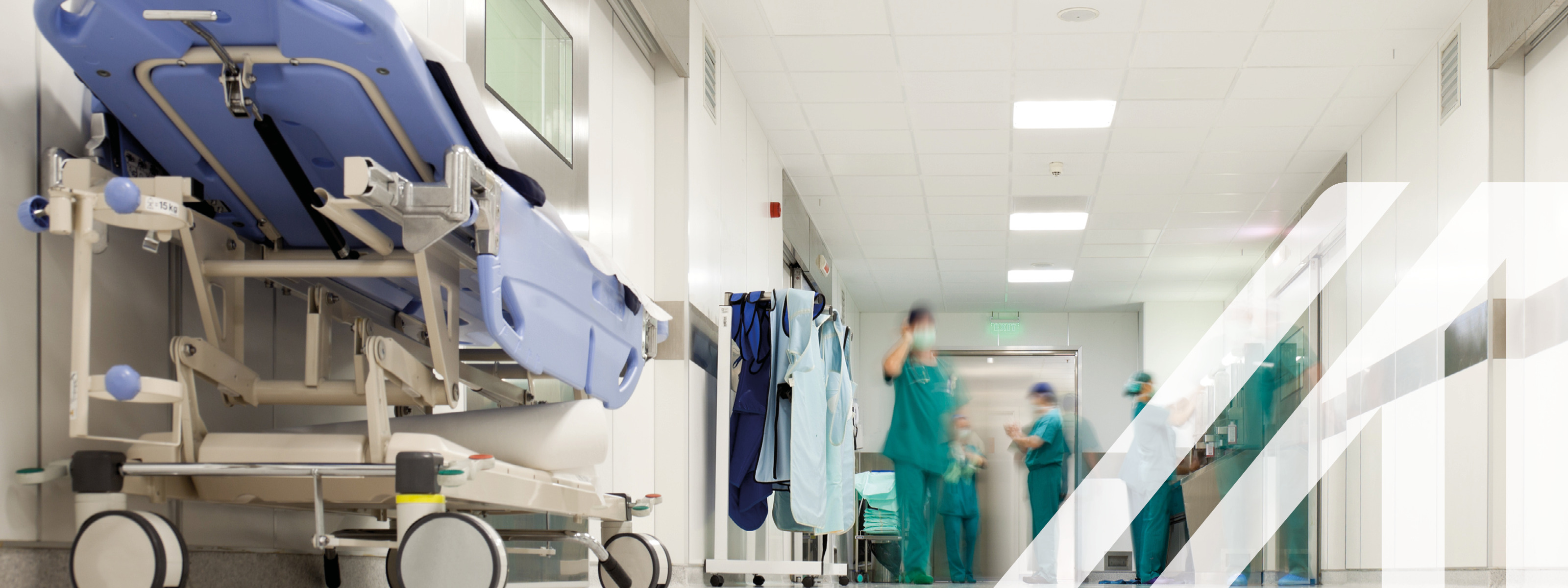 Weißer Korridor eines Krankenhauses mit Krankenhausbett und medizinischem Personal in grüner OP-Kleidung