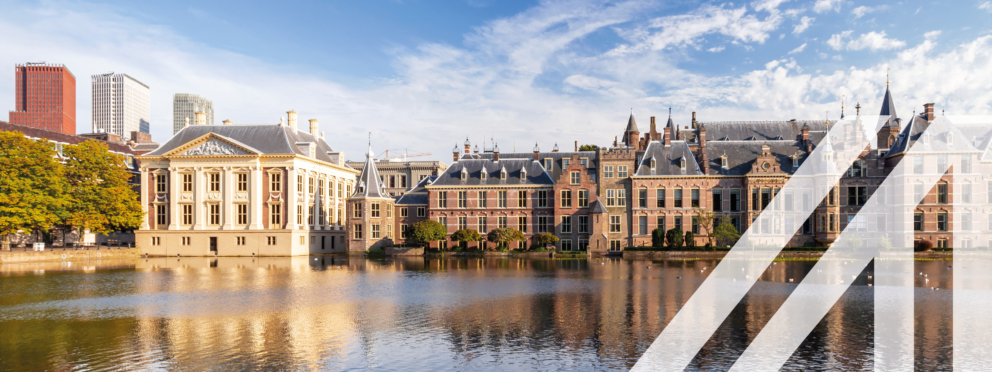 Blick auf den Binnenhof, das niederländische Parlament in Den Haag, historische Häuser gelegen am Wasser unter blauem Himmel. Über das Bild wurde ein weißes Austria A gelegt.