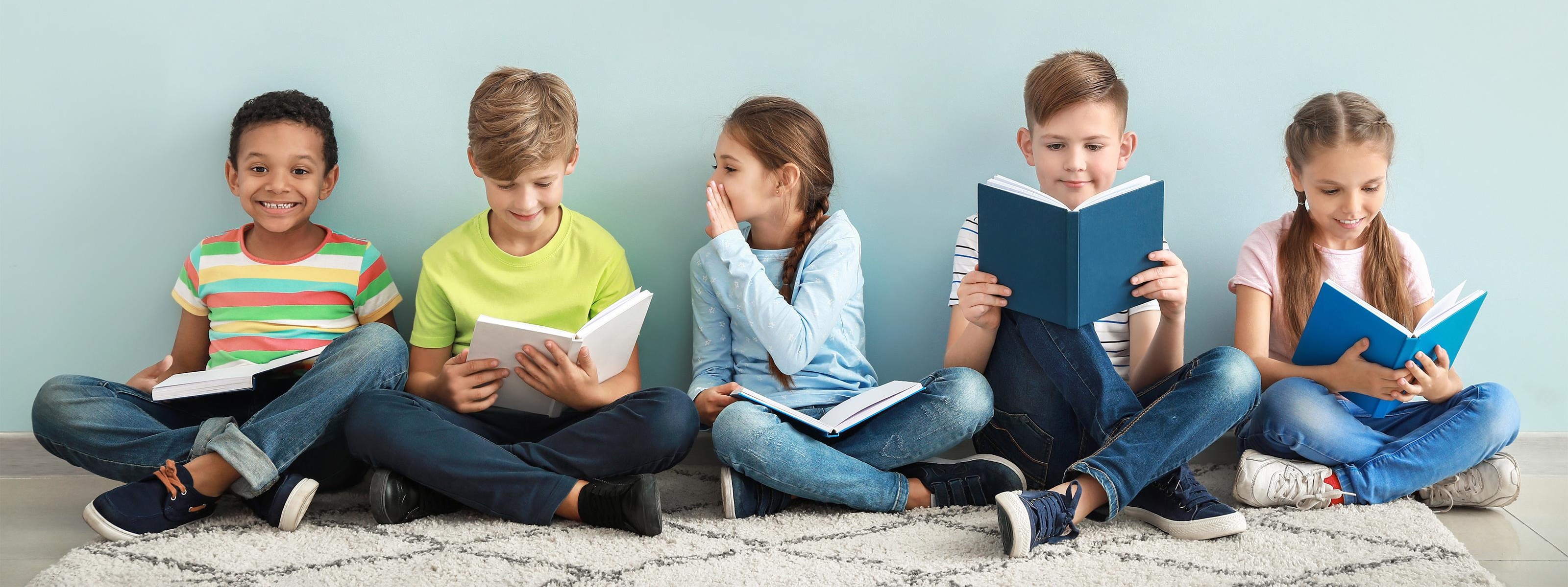 Fünf Kinder sitzen in einer Reihe im Schneidersitz und lesen Bücher