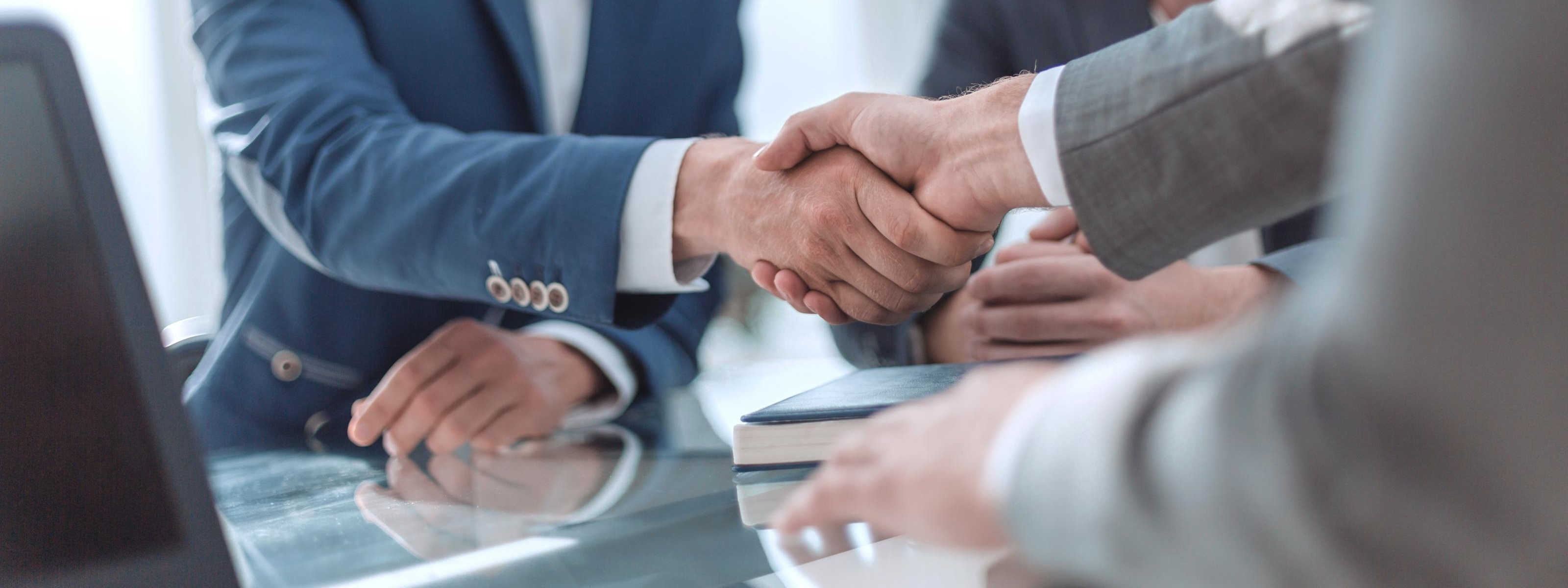 Händeschütteln im Fokus, zwei Personen im Anzug lächeln Hand gebende Person an
