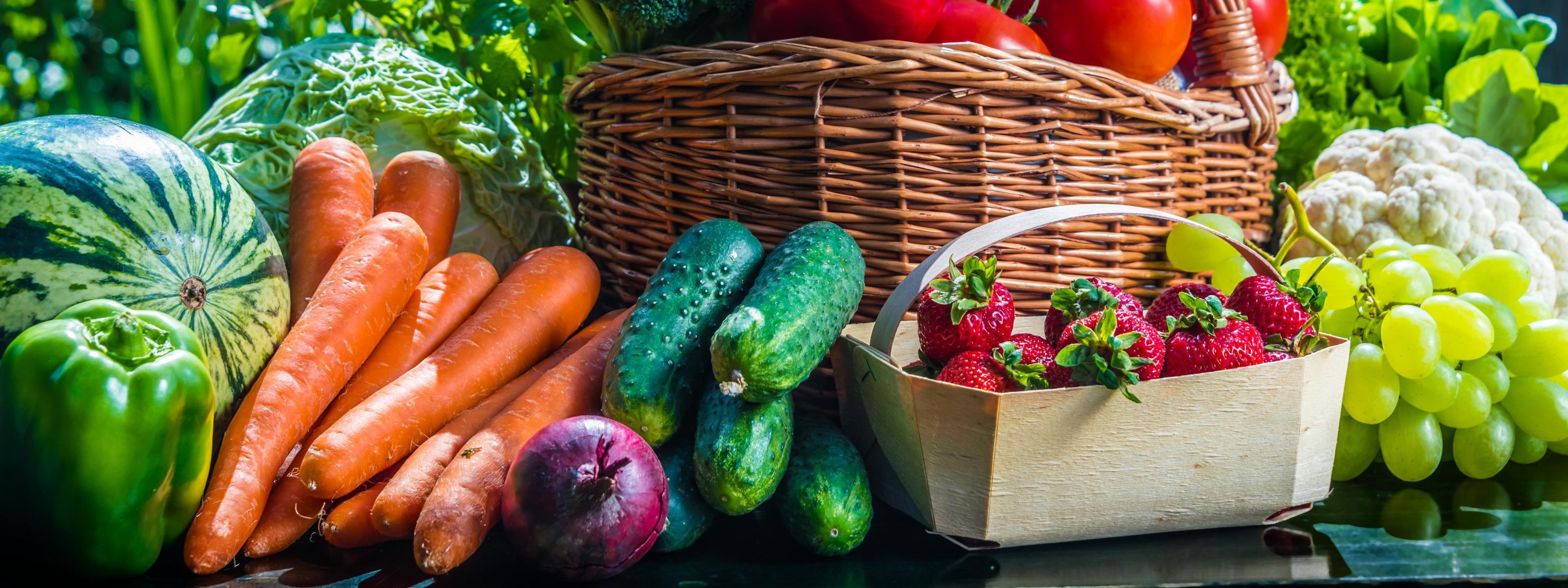Variation von verschiedenen Obst- und Gemüsesorten lose oder in Gebinden auf einem Tisch im Freien, im Hintergrund grünes Bokeh
