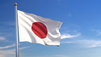 Die Flagge des Landes Japan weht an einem Mast angebracht im Wind. Im Hintergrund ist blauer Himmel mit vereinzelten Wolken zu sehen.