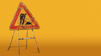 Vor gelbem Hintergrund ist ein dreieckiges Schild, auf dem die Silhouette einer Person eine Schaufel hält und sich nach vorne beugt. Vor ihr liegt ein Haufen