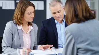 Drei Personen sitzen an einem Tisch bei einer Besprechung