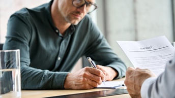 Person mit Brillen unterfertigt Dokument, Ausschnitt anderer Person, die Dokument mit Schriftzug Contract in Händen hält 