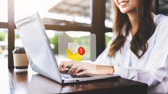 Eine junge Frau vor ihrem Laptop - darüber ein E-Mail-Zeichen