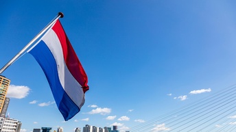 Die Flagge der Niederlande im Wind wehend vor einer Stadtansicht Rotterdams vom Fluss aus.