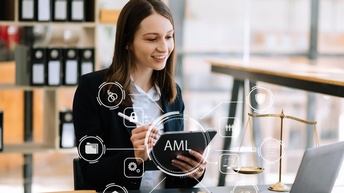 Eine Person sitzt an einem Tisch. In den Händen hält sie ein Tablet. Vor ihr ist ein aufgeklappter Laptop. Overlay diverser Symbole: Über der Person in der Mitte steht AML. Um AML sind verschiedene Symbole angelegt wie Zahnräder, eine Waage, ein Schloss.