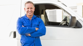 Lächelnde Person in blauem Hemd lehnt an weißem Transportwagen