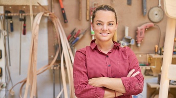 Lächelnde Person steht mit verschränkten Armen in Werkstatt