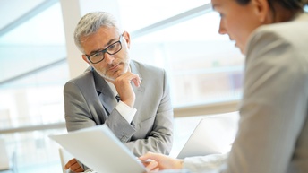 Zwei Personen sitzen an Tisch und blicken auf Dokument