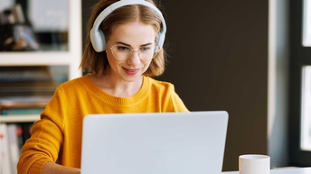 Junge Frau mit einem Gelben Pullover und Kopfhörern sitzt vor einem Laptop