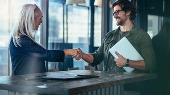 Zwei lächelnde Personen reichen sich über Stehtisch die Hand