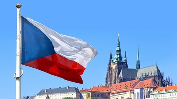 Die Flagge Tschechiens im Wind wehend unter blauem Himmel vor einer Stadtansicht Prags.