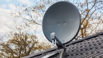 Eine Satellitenschüssel auf dem schrägen Dach eines Hauses