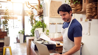 Person blickt auf einen aufgeklappten Laptop in einem Lokal