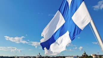 Die finnische Flagge weht im Wind, im Hintergrund eine Stadtansicht.