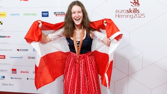Katharina Höller, lachend, mit Medaille und Österreich-Flagge um die Schultern