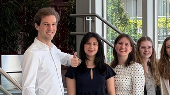 Gruppenfoto von acht Personen in Bürokleidung, die nebeneinander vor einem großen rot-weiß-roten A in einem Gang stehen