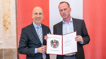 Bundesminister Martin Kocher und Joachim Tiefenbacher halten eine Urkunde