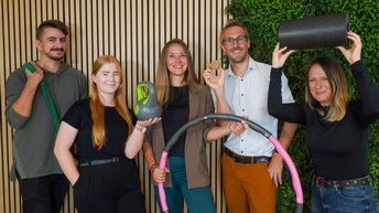 Männer und Frauen präsentieren unterschiedliche Sportgeräte wie Hula-Hoop-Reifen, Kettlebell oder Faszienrolle