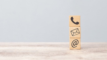 Drei Holzwürfel aufeinander gestapelt mit Kontaktsymbolen Telefonhörer, Briefumschlag und @