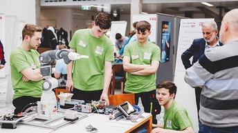 Personen unterschiedlichen Alters rund um einen Roboterarm.