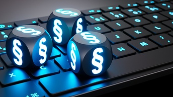 Nahaufnahme einer Computertastatur auf grauem Untergrund stehend. Auf der Tastatur liegen drei Würfel. Auf jeder Seite eines jeden Würfels ist ein leuchtendes Paragraph-Symbol