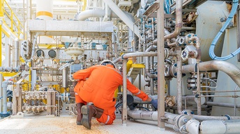 Person in orangem Schutzanzug in Rückenansicht kontrolliert auf Boden kniend Leitungen