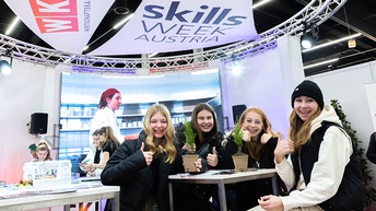 Mehrere lächelnde junge Personen um Tisch stehend mit Daumen nach oben, über ihnen der Schriftzug Skills Week Austria