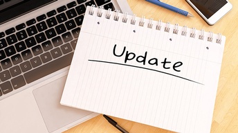 Notizblock mit Schriftzug Update liegt auf Computertastatur, daneben Stifte und ein Smartphone.