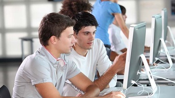 Zwei Personen sitzen vor Computerbildschirm