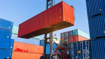 Fahrzeug umgeben von Transportcontainern hievt roten Transportcontainer in die Luft