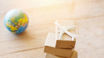  Miniaturpakete mit einem Miniaturflugzeug sind auf einem Holzuntergrund platziert, daneben ist ebenso ein Miniaturglobus