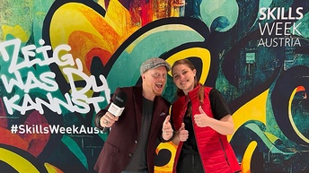 Zwei Personen mit nach oben gestreckten Daumen vor Grafitiwand mit Schriftzügen Zeig, was du kannst und Skills Week Austria