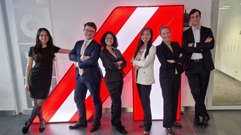 Gruppenfoto von sechs Personen in Bürokleidung, die nebeneinander vor einem großen rot-weiß-roten A in einem Gang stehen