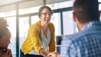 Lächelnde Person mit Brille in gelber Jacke mit Tätowierung am Unterarm schüttelt anderer Person die Hand