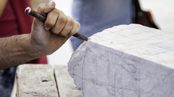 Hand mit Meißel, die einen Stein bearbeitet.