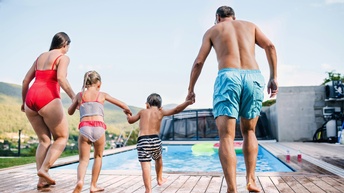 Zwei Erwachsene und zwei Kinder halten sich an den Händen und laufen auf einen Pool zu 