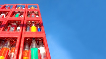 Turm aus roten mit Plastikflaschen gefüllten Getränkekisten unter blauem Himmel