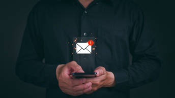 Frontale Aufnahme einer Person, die ein Smartphone hält. Über dem Smartphone ist ein Icon eines Briefumschlags. An der rechten oberen Ecke des Briefumschlags ist eine weiße eins in einem roten Kreis