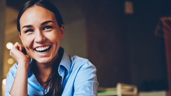Lachende Person in blaugestreiftem Hemd stützt einen Arm an die Wange, der andere Arm am Tisch abgestützt mit iWatch am Handgelenk