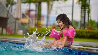 Mädchen sitzt mit Schwimmflügel an einem Schwimmbeckenrand