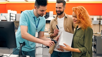 Drei Personen in Elektrofachgeschäft: Eine Person scannt Box, die andere Person in Händen hält