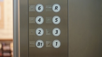 Nahaufnahme von Stockwerkknöpfen in einem Aufzug, daneben ist jeweils die Brailleschrift angegeben